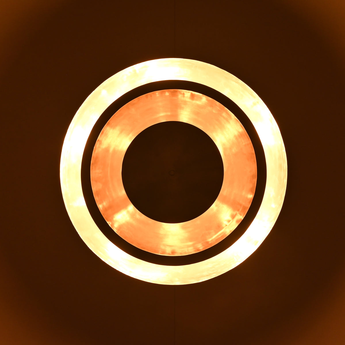 Glowing top view of a circular tiered disc light with bright illuminated rings and handcrafted metallic finish.