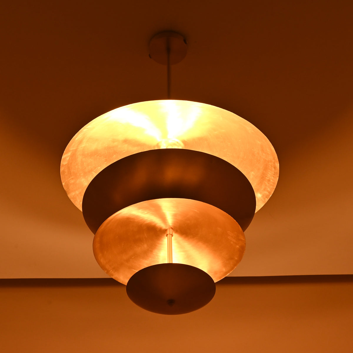Triple disc brass chandelier illuminated, showcasing warm ambient brass reflection on ceiling