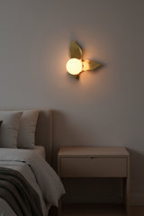 Brass leaves glass globe wall sconce shown from front with artistic folded brass panels and soft warm light