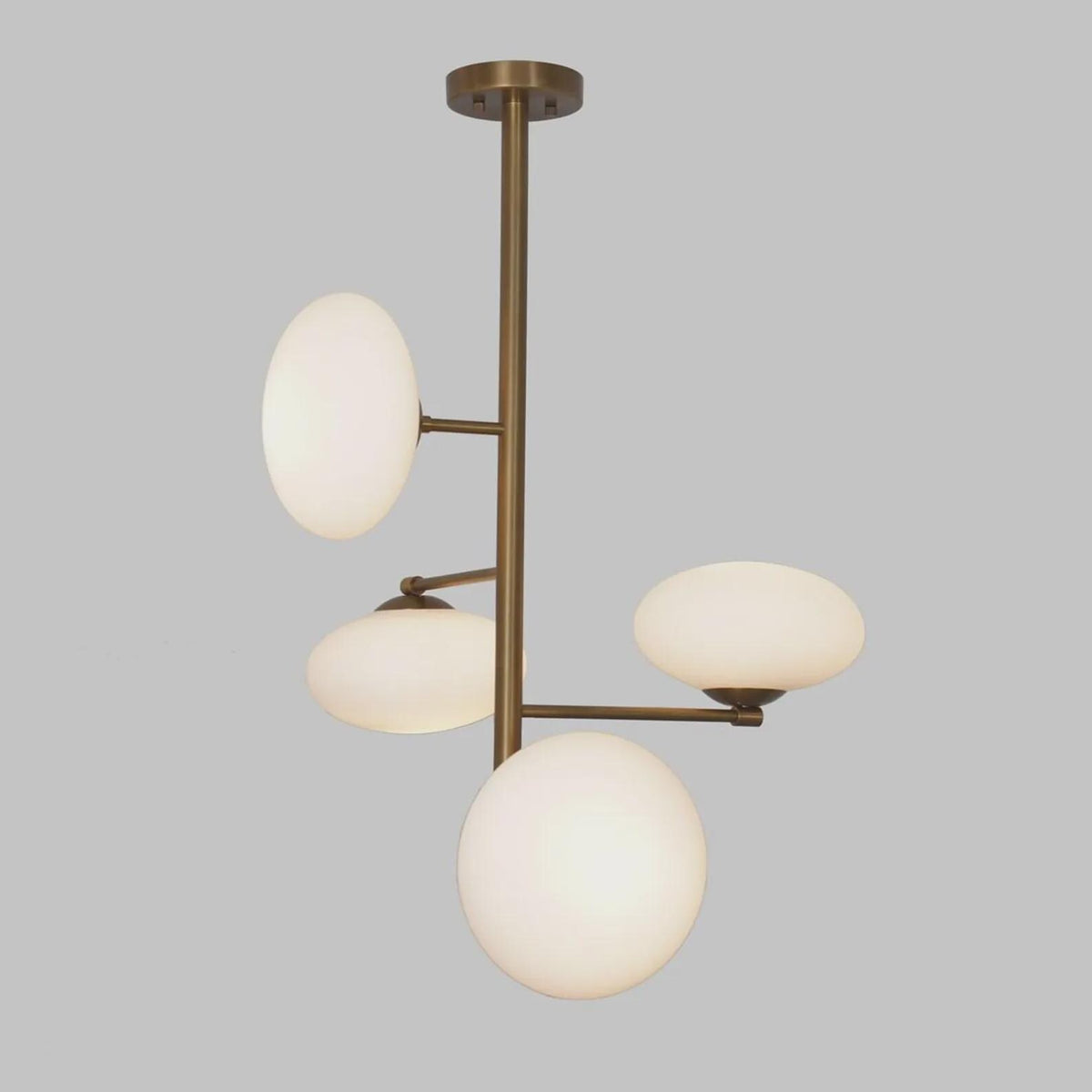 Front view of a handcrafted brass chandelier with four milky glass globes, showcasing balanced proportions and minimalist industrial style.