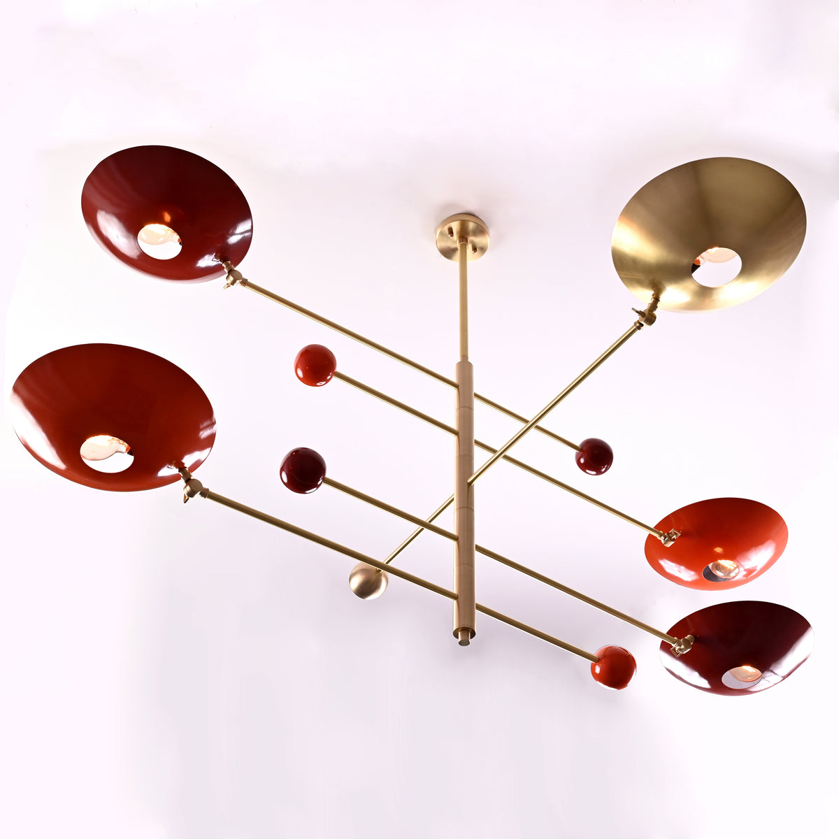 Brass mobile chandelier with modern geometric design and red bowl-shaped uplight shades handcrafted by Brass Leaf Studio.