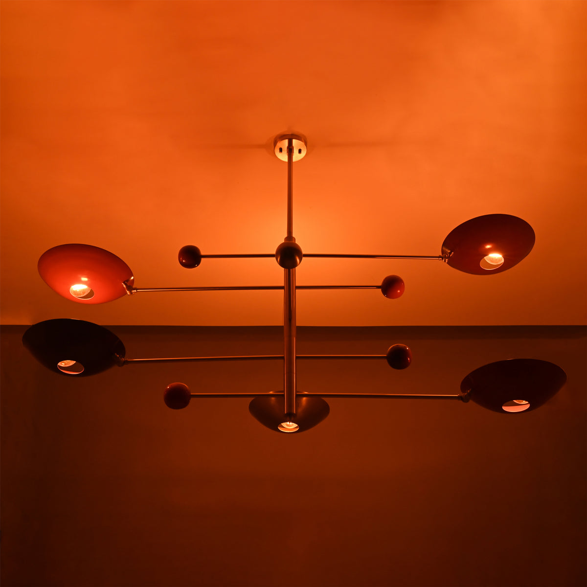 Brass mobile chandelier illuminated in warm ambient light, showcasing sculptural arms and red reflective bowl shades.