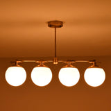 Front-facing view of brass linear chandelier with four opal glass globes in a low-light interior setting.