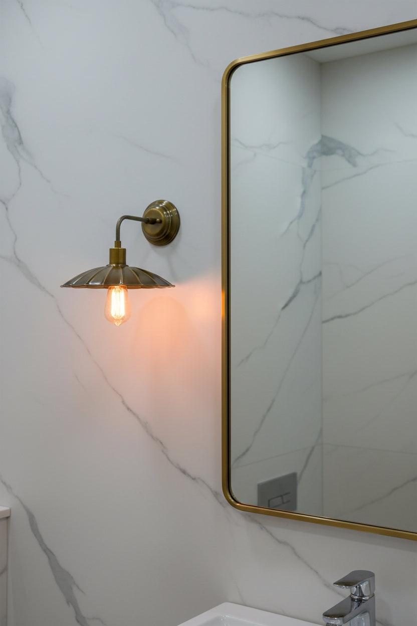 Brass patina bedroom wall sconce with curved arm, round backplate, and scalloped brass shade