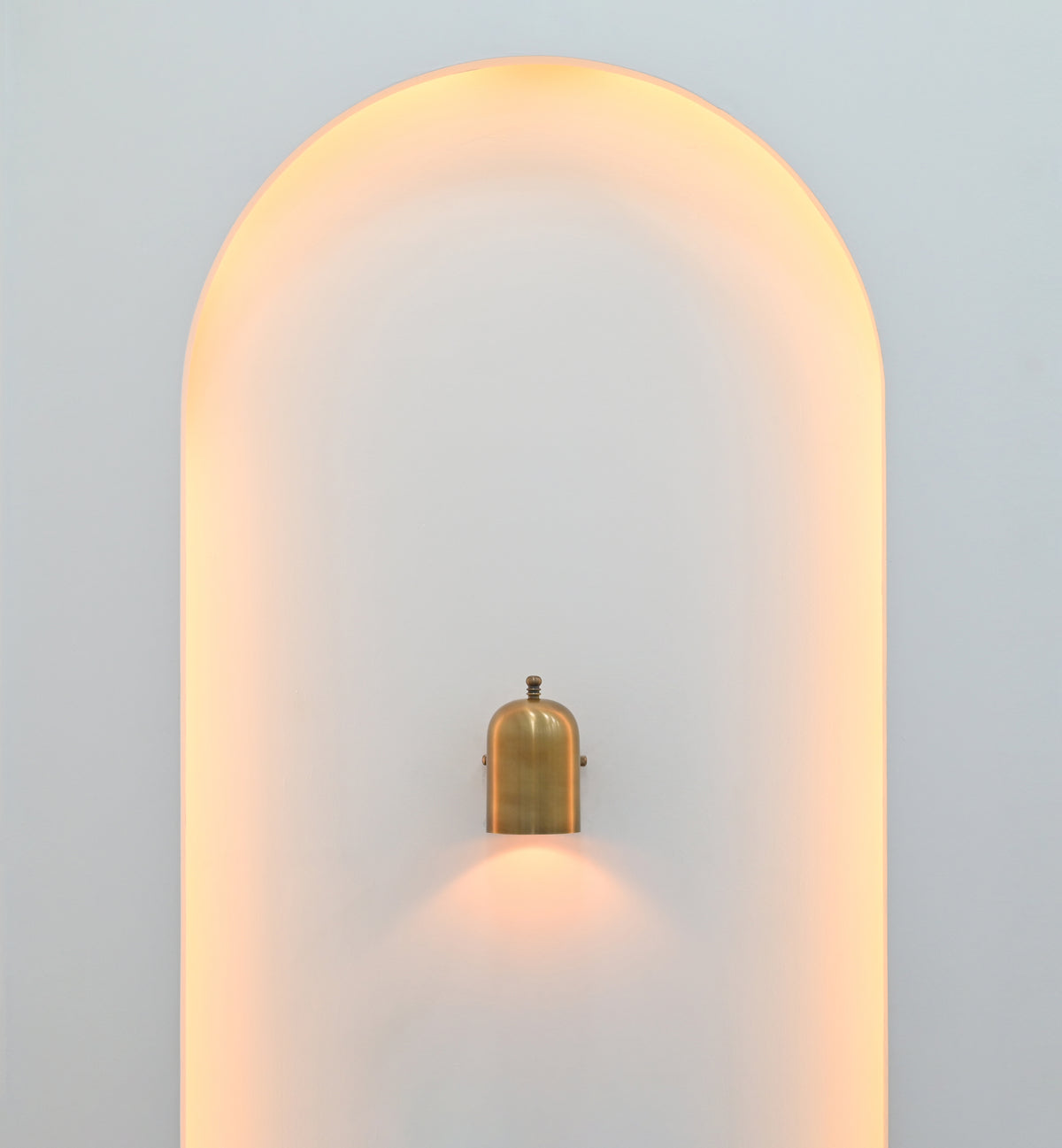 Cylindrical wall light in brass patina finish creating warm focused downward illumination on a light-colored wall