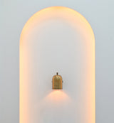 Cylindrical wall light in brass patina finish creating warm focused downward illumination on a light-colored wall
