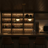 Closeup of brass patina pendant lamp showing curved arm detail, cone shades, and glowing globe lights