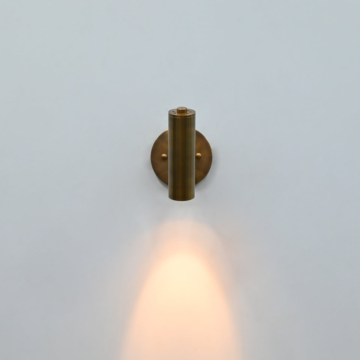 Side view of brass patina cylindrical wall sconce with adjustable-style support arm and round mounting plate