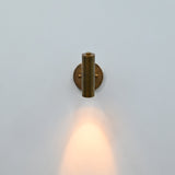 Side view of brass patina cylindrical wall sconce with adjustable-style support arm and round mounting plate