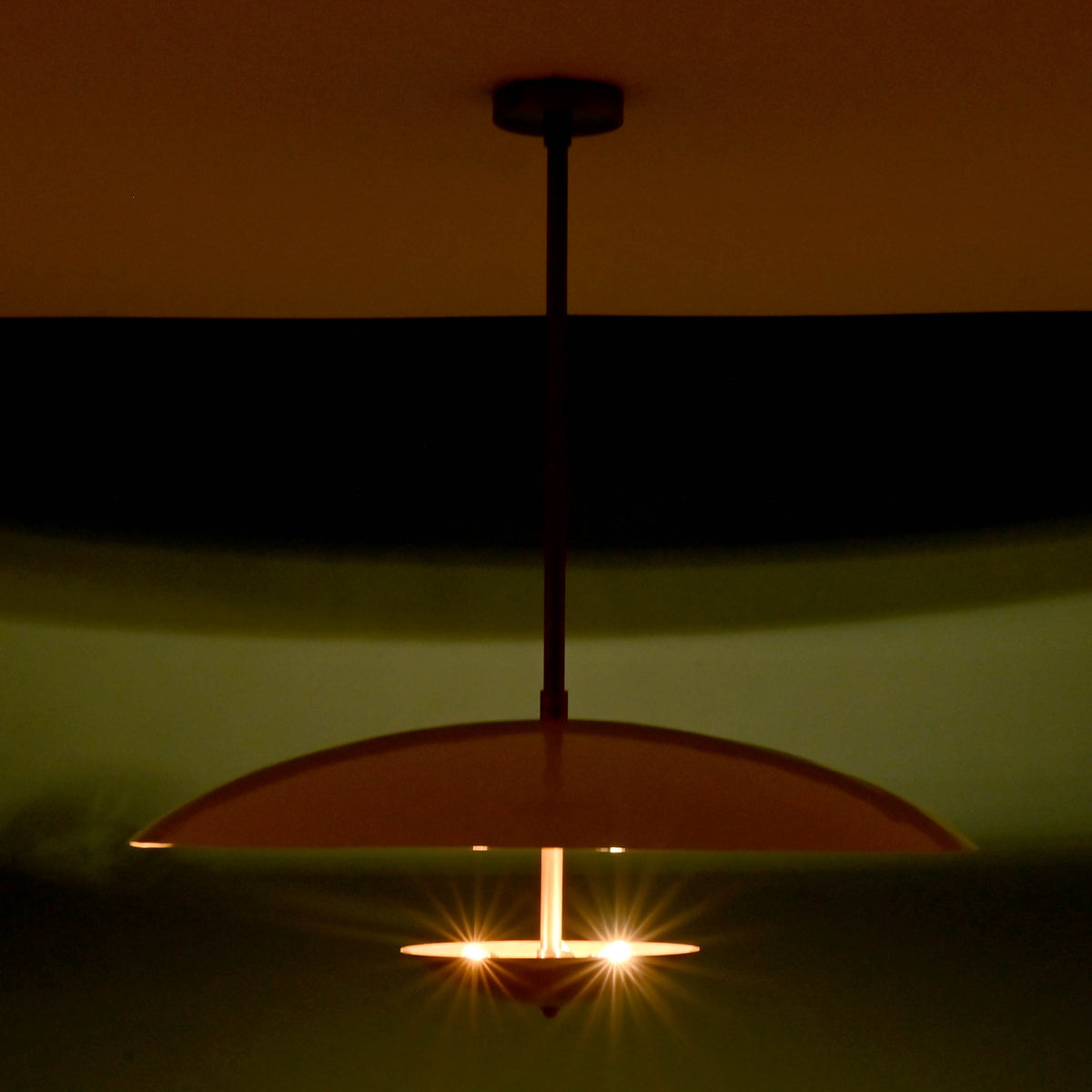 Handmade brass pendant lamp glowing warmly in a dark room, creating a sculpted light effect with elegant ambient illumination.