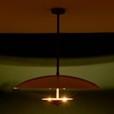 Handmade brass pendant lamp glowing warmly in a dark room, creating a sculpted light effect with elegant ambient illumination.