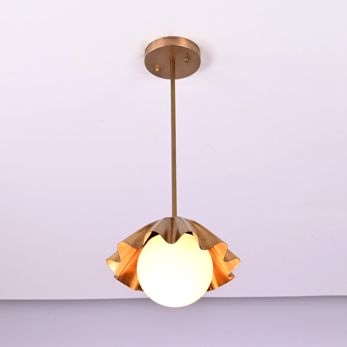 Angled view of handmade brass ruffled pendant lamp with frosted globe bulb