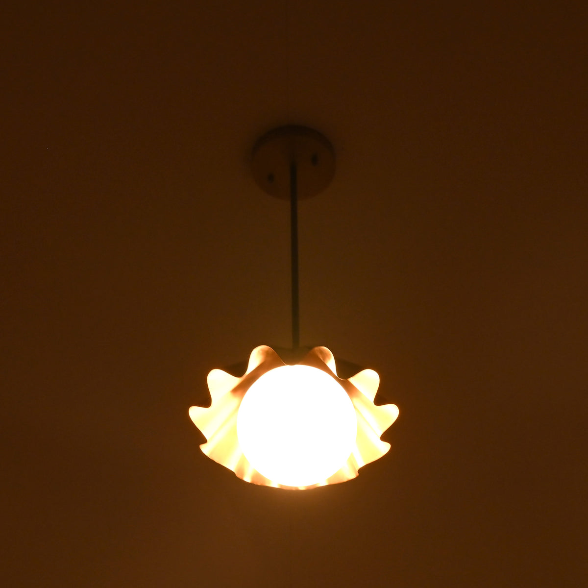 Brass pendant chandelier with ruffled shade glowing warmly in a dark interior