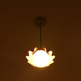 Brass pendant chandelier with ruffled shade glowing warmly in a dark interior