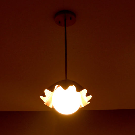 Warm glowing brass pendant light with ruffled shade and frosted bulb in a dimly lit room