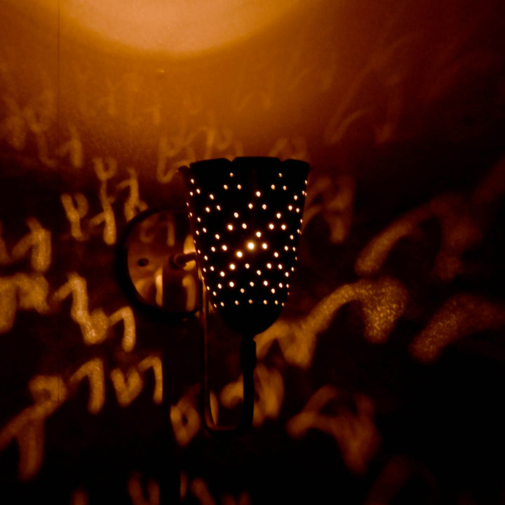 Handmade brass wall sconce casting intricate light pattern in dark space