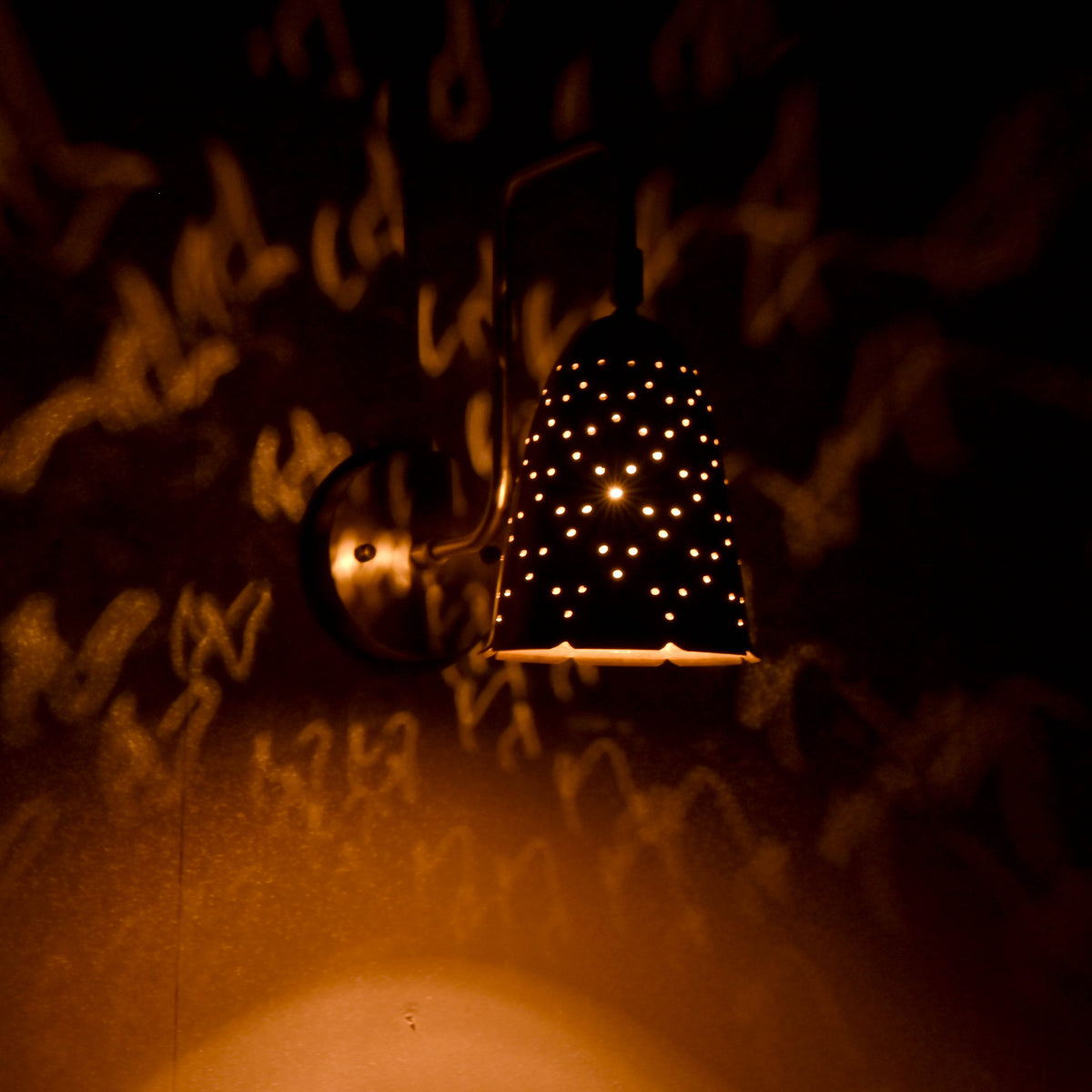 Brass perforated wall sconce creating artistic golden light patterns on wall