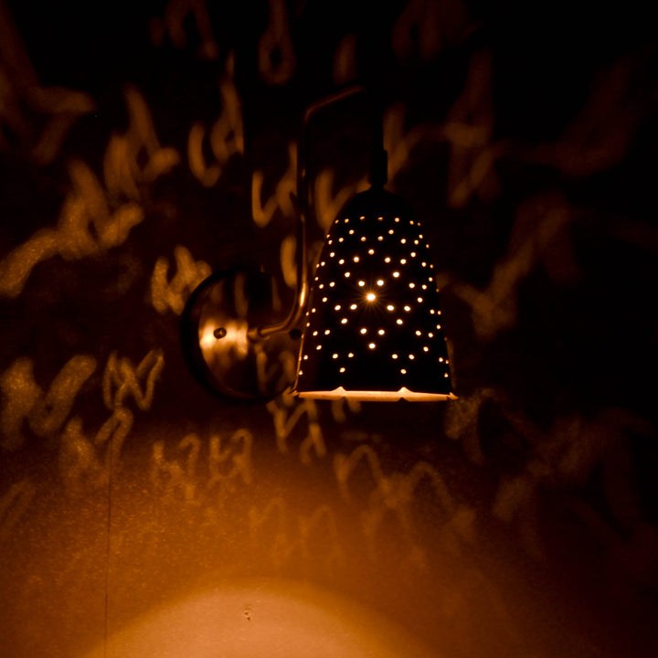 Brass perforated wall sconce creating artistic golden light patterns on wall