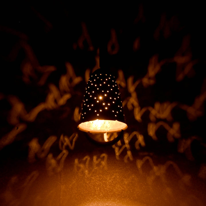 Brass perforated wall sconce glowing in dark room with decorative light shadows