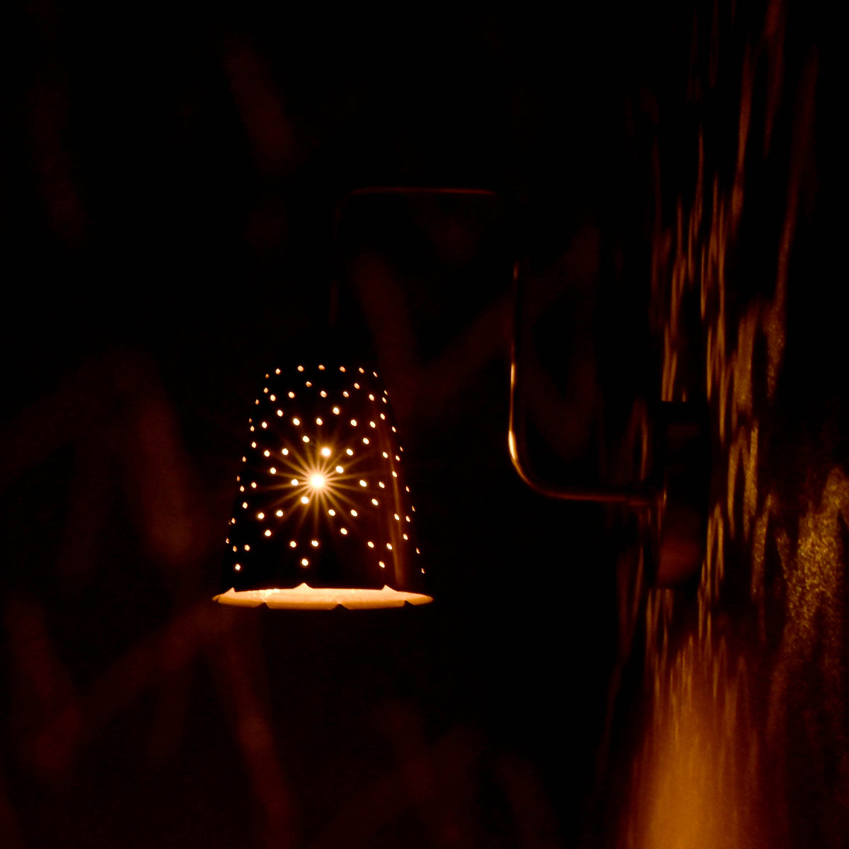 rass perforated sconce light creating starburst glow effect on wall in dark
