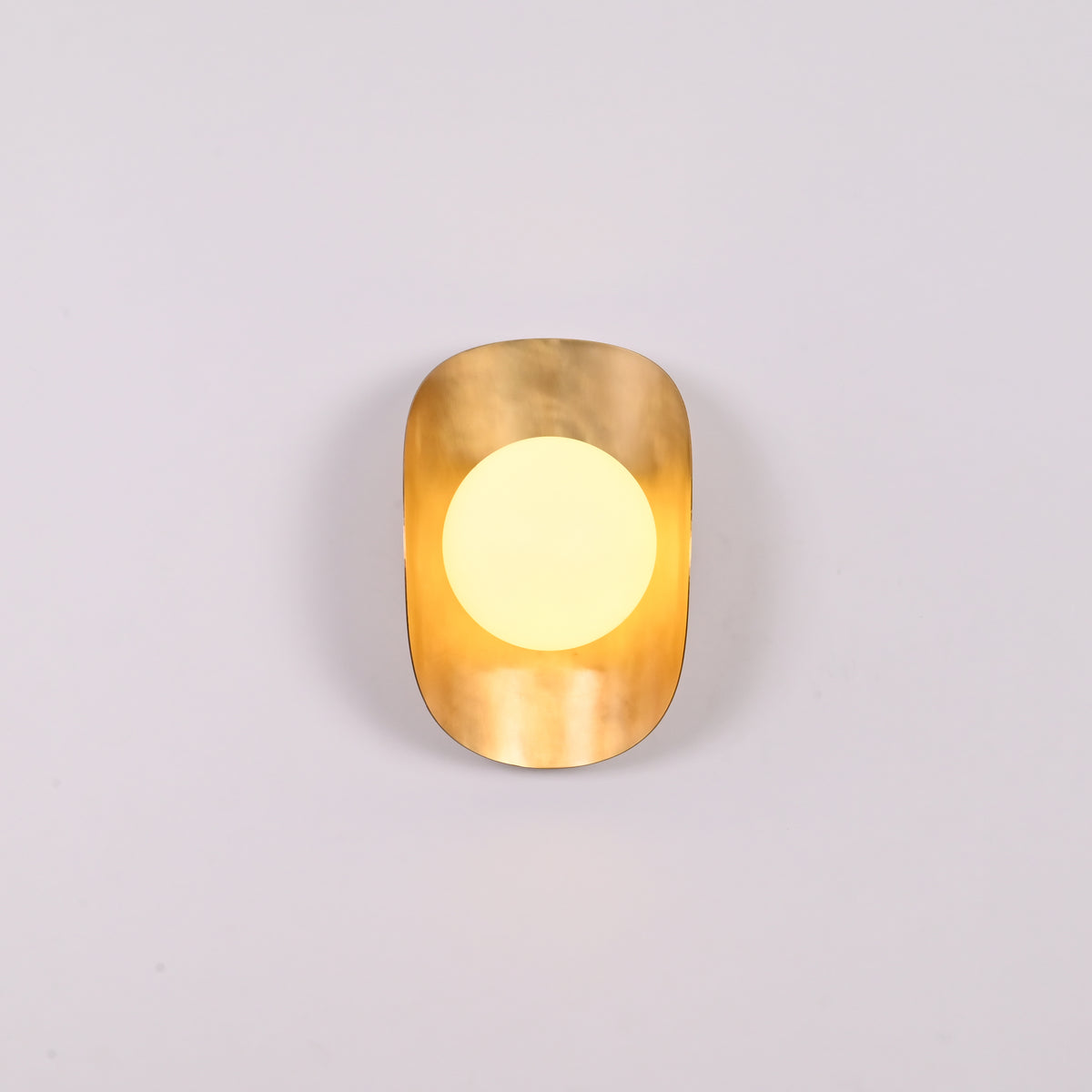 Brass shield globe sconce creating soft warm glow for luxury home and boutique interiors