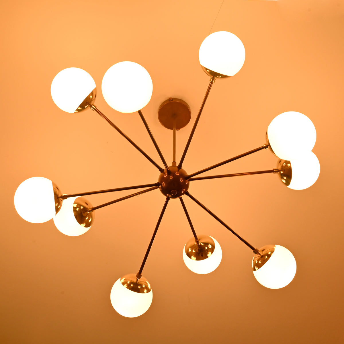 Bottom view of illuminated brass Sputnik chandelier with opal glass globes on a warm ceiling.