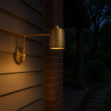Brass swing arm wall sconce with perforated shade providing warm ambient lighting on exterior wall