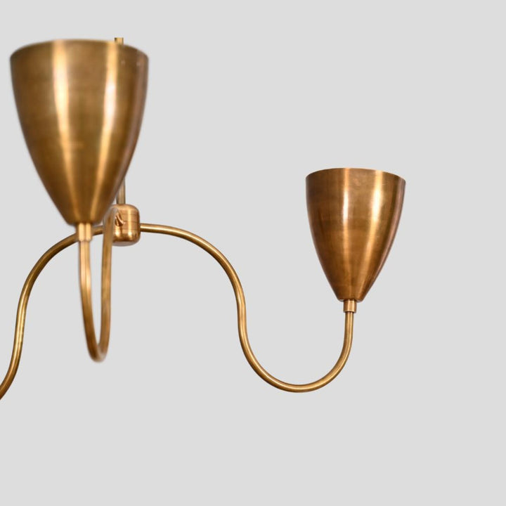 Close-up of brass chandelier showing detailed curved arm and conical shade design, handcrafted minimalist industrial ceiling light.