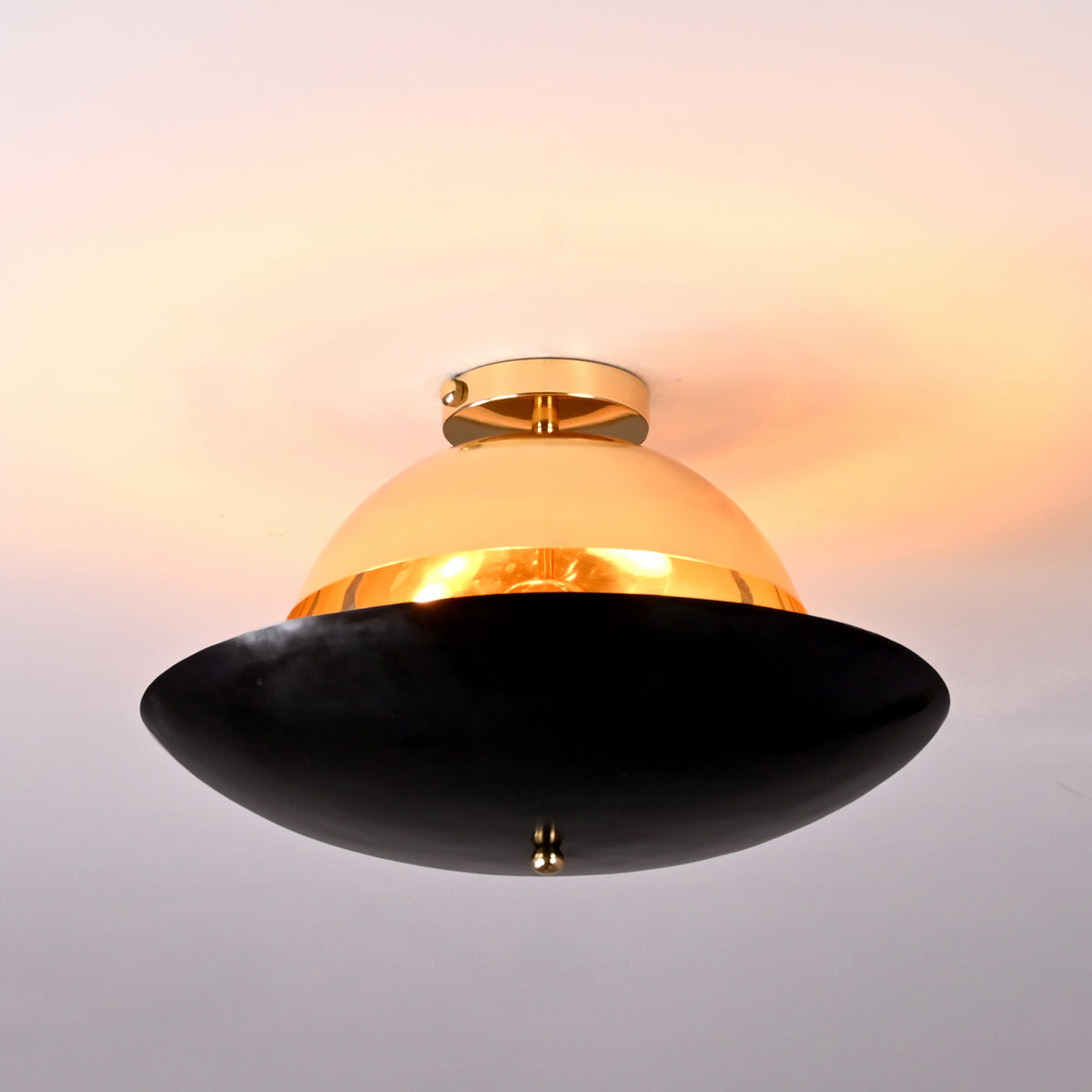 Two-tone brass flushmount light glowing warmly, showing polished brass upper shade and dark lower bowl with soft ambient lighting.