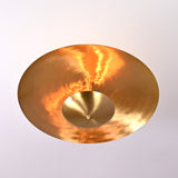 Bottom view of brass disc chandelier showing glowing indirect light and hammered brass reflection