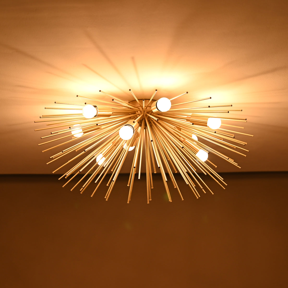 Brass urchin chandelier lit in a dark room, casting dramatic warm light patterns across the ceiling.