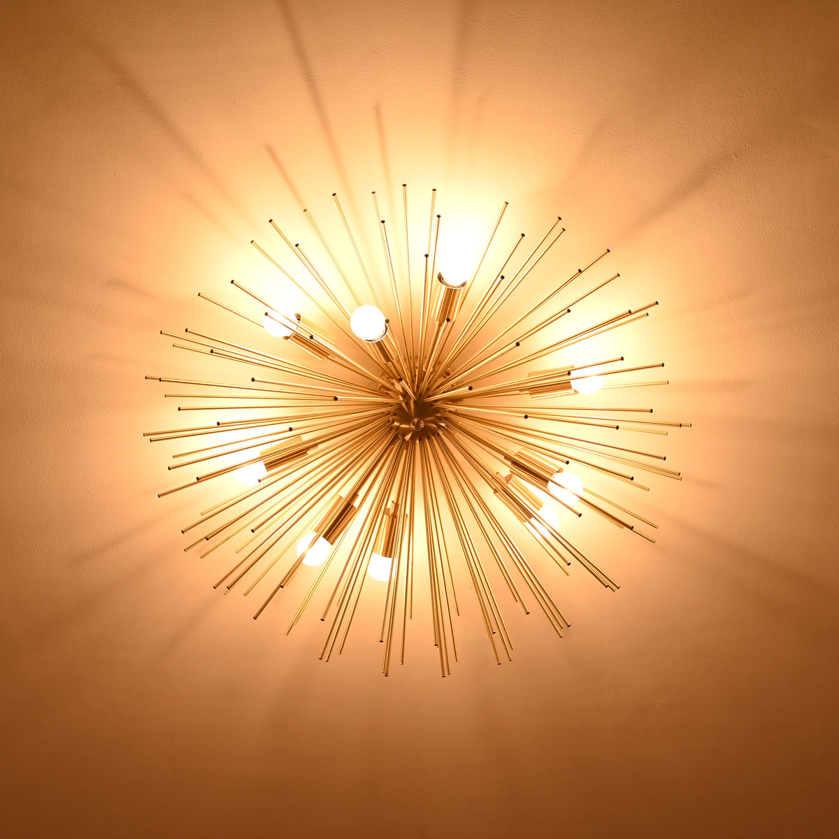 Warm-toned bottom shot of brass urchin chandelier highlighting extended brass rods and glowing bulbs.