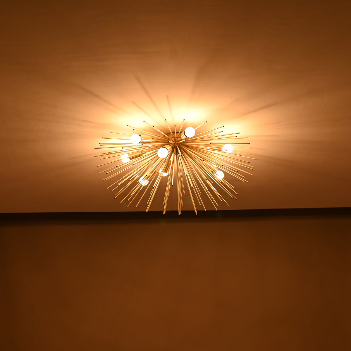 Wide room view of brass urchin chandelier casting ambient warm light and radial shadow patterns.