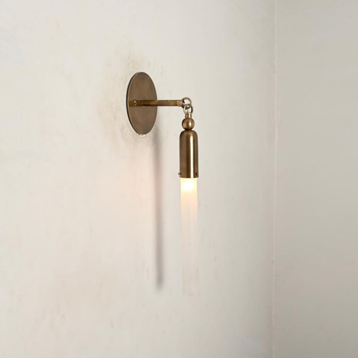 Handmade brass vertical wall light with slim frosted glass tube shade, industrial minimalist sconce angled view