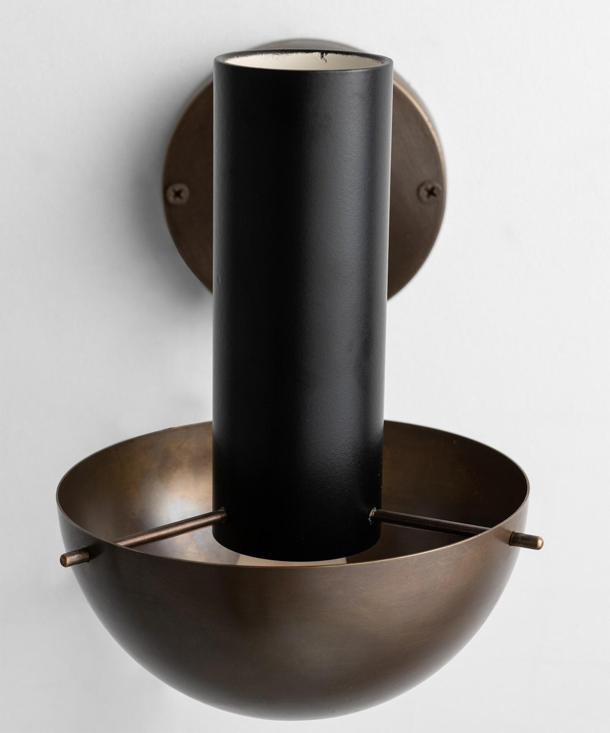 Close-up of brass wall lamp showing cylindrical upper form, solid brass wall mount, and hand-finished surface detailing.