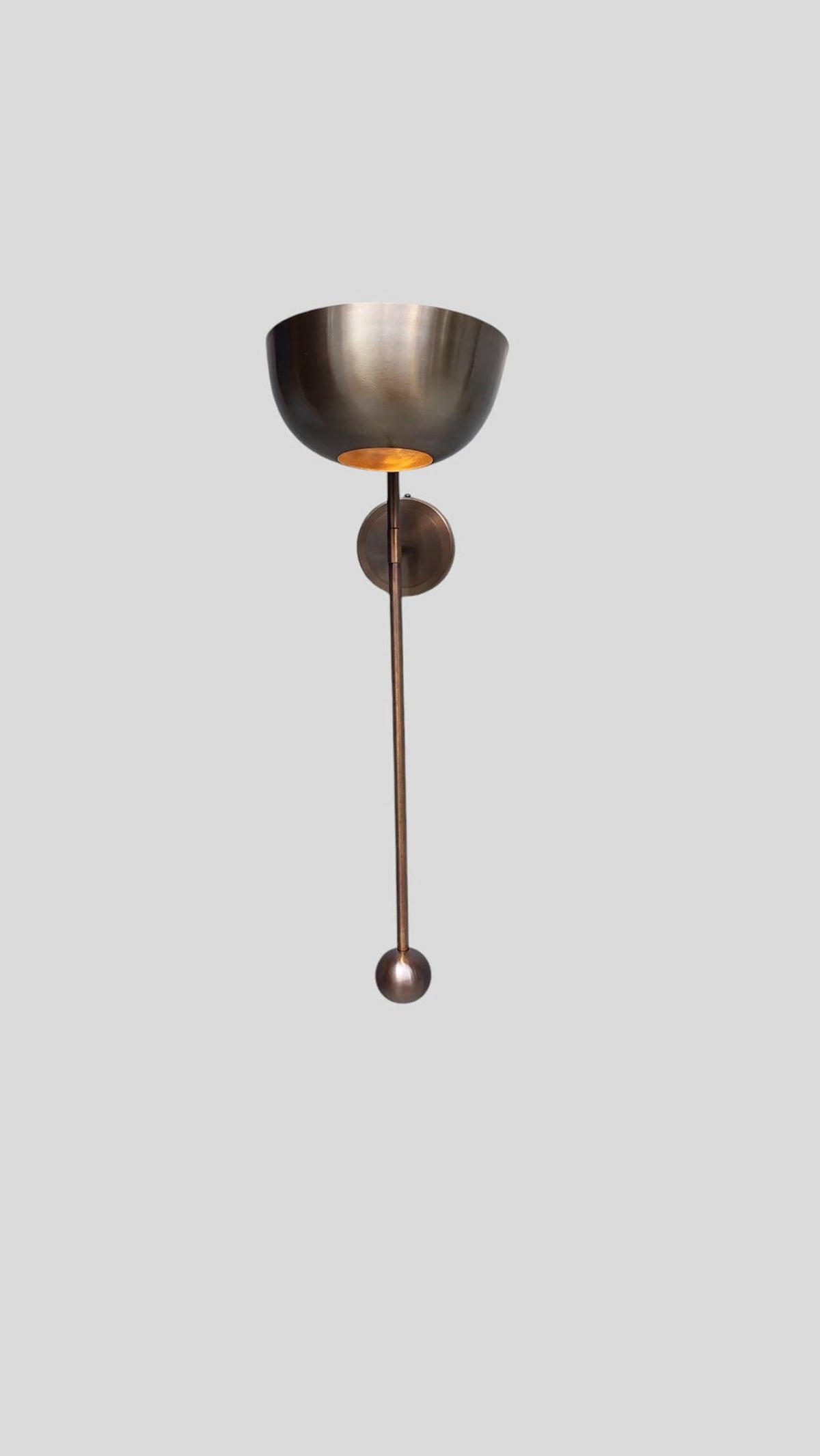 Full height view of brass wall sconce with round bowl shade and extended rod