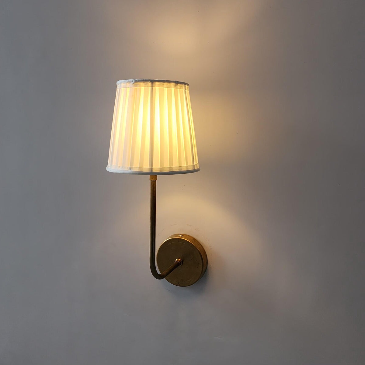 Side view of brass wall light featuring a pleated fabric shade and warm diffused glow.