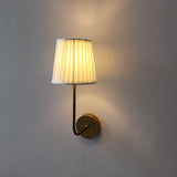 Side view of brass wall light featuring a pleated fabric shade and warm diffused glow.