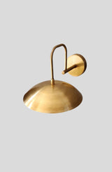 Back angle of brass wall light fixture showing round wall mount and curved arm