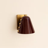 Side view of burgundy cone wall sconce with decorative brass studs and square brass backplate
