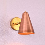 Brass wall sconce with conical copper shade, mounted on a round brass base, minimalist design for modern interiors.