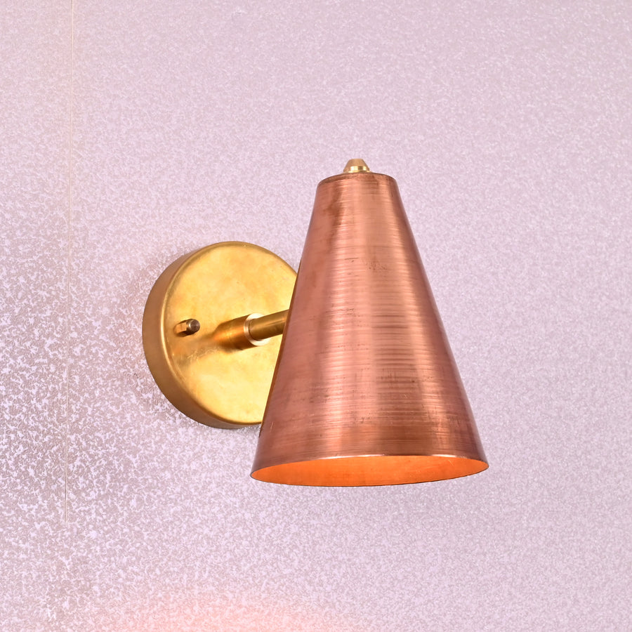 Brass wall sconce with conical copper shade, mounted on a round brass base, minimalist design for modern interiors.