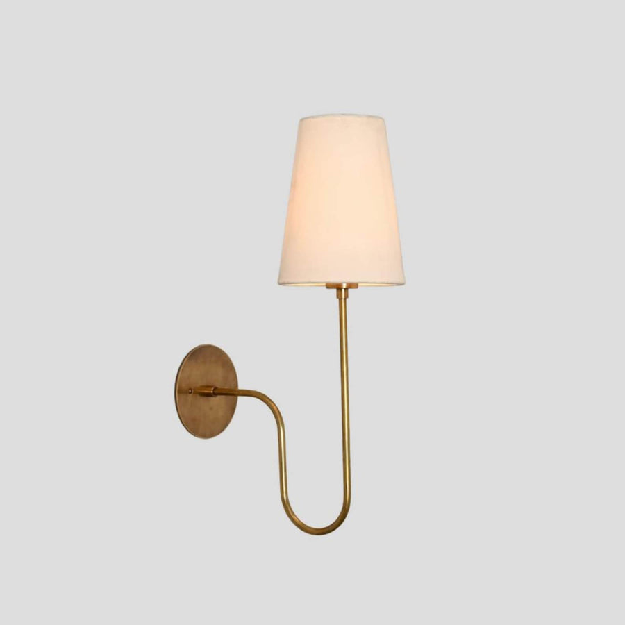 Handmade brass wall sconce with elegant curved arm and tapered fabric shade, designed for modern and classic interiors.