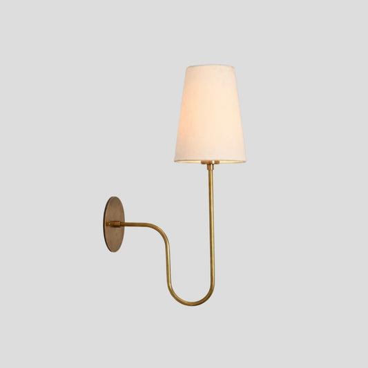 Elegant brass wall lamp with slim curved arm and white fabric shade, perfect for bedrooms, dining areas, and boutique interiors.