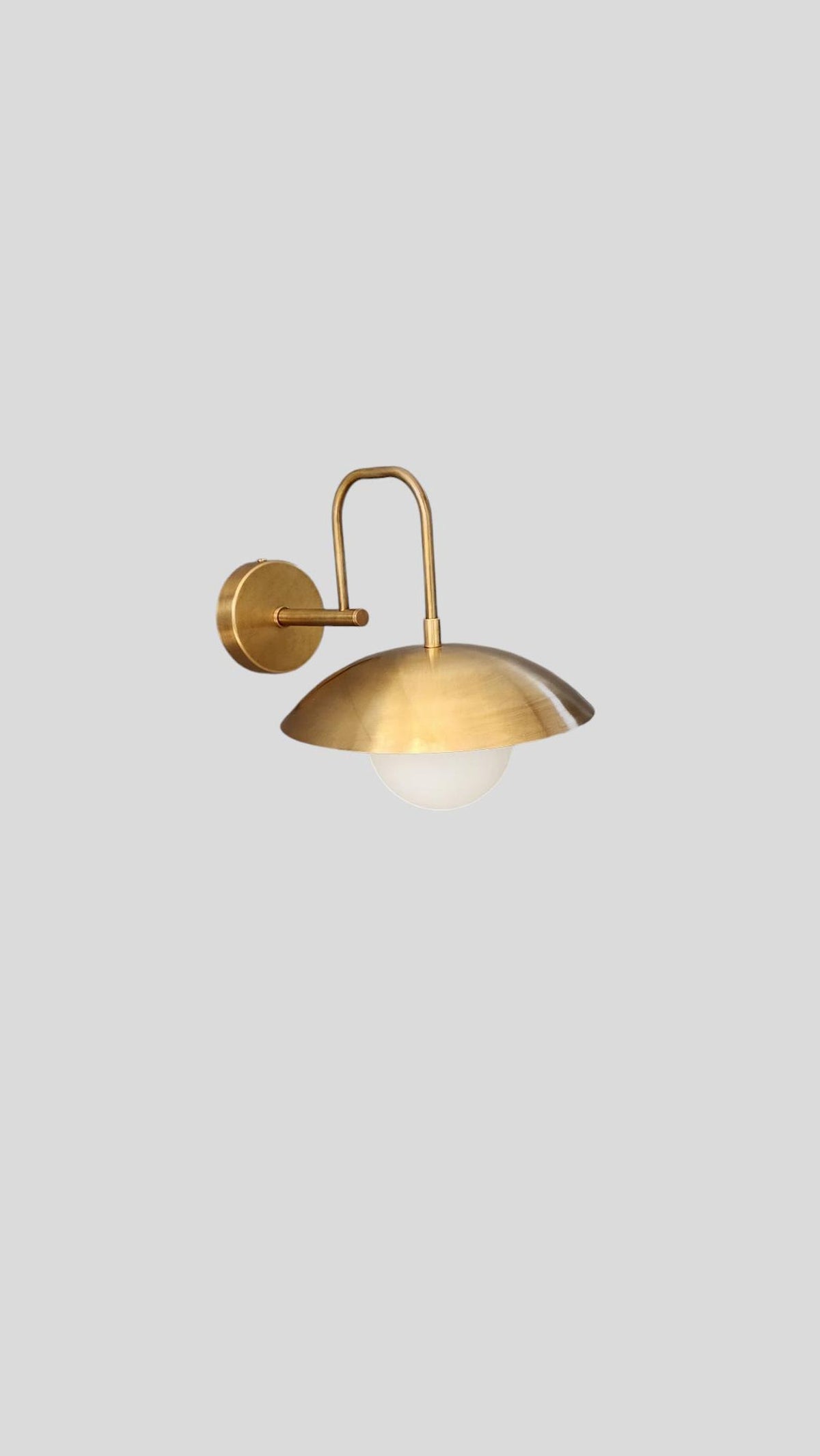 Full view of brass wall-mounted sconce with minimalist industrial design and globe shade