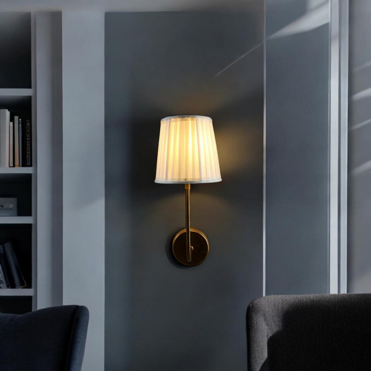 Brass wall sconce with white pleated shade mounted in a modern living room interior.