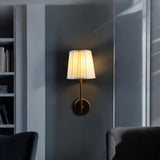 Brass wall sconce with white pleated shade mounted in a modern living room interior.