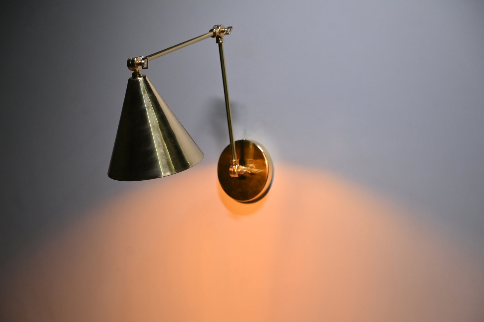 Handmade brass wall sconce with cone shade casting warm downward glow