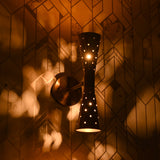 Close-up of brass double cone wall sconce lit, casting warm patterned light on wall