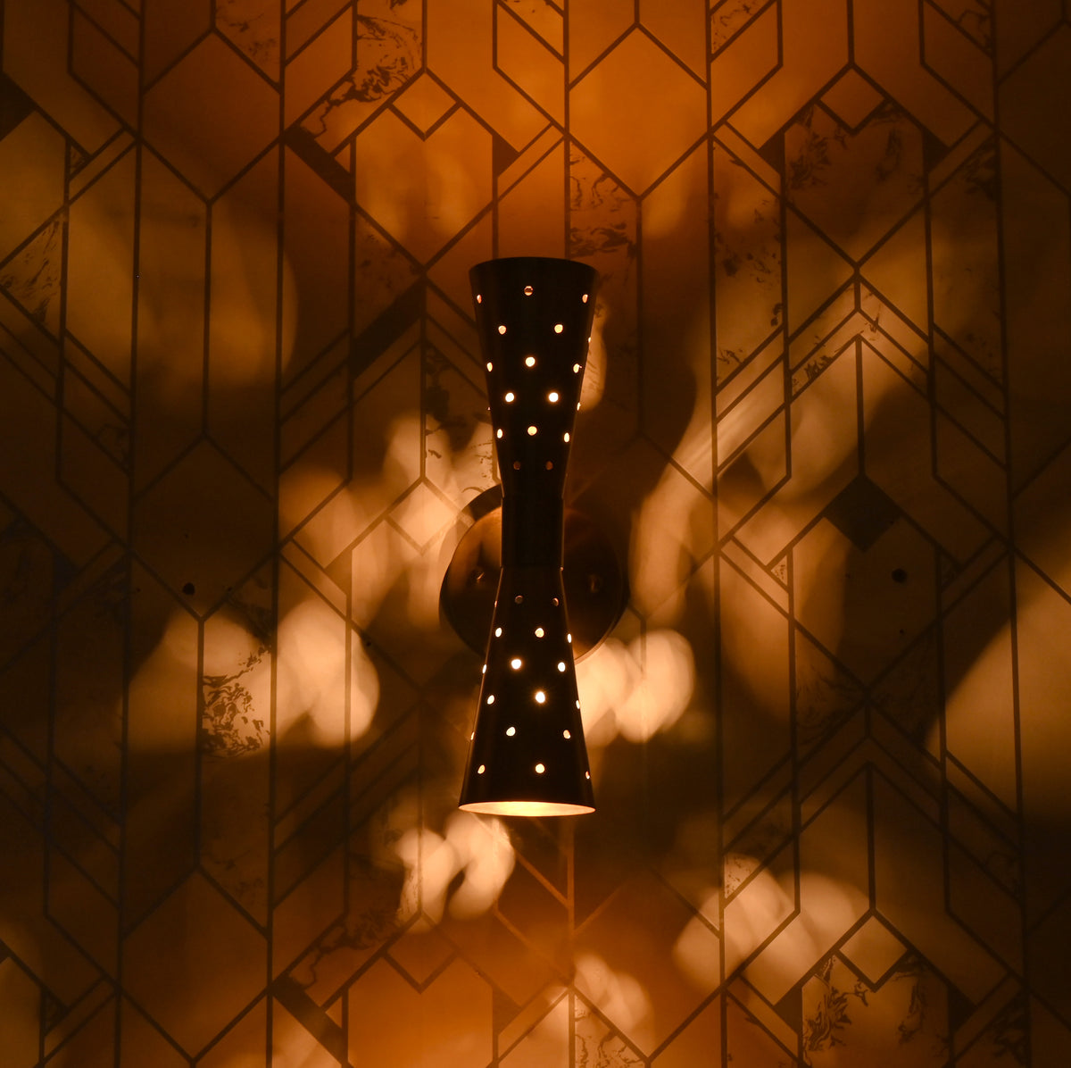 Brass double cone wall sconce illuminated, creating decorative light patterns on wall